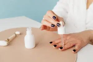 Blog Articles Close-up of a woman applying nail oil with a dropper for manicure care on blue background.